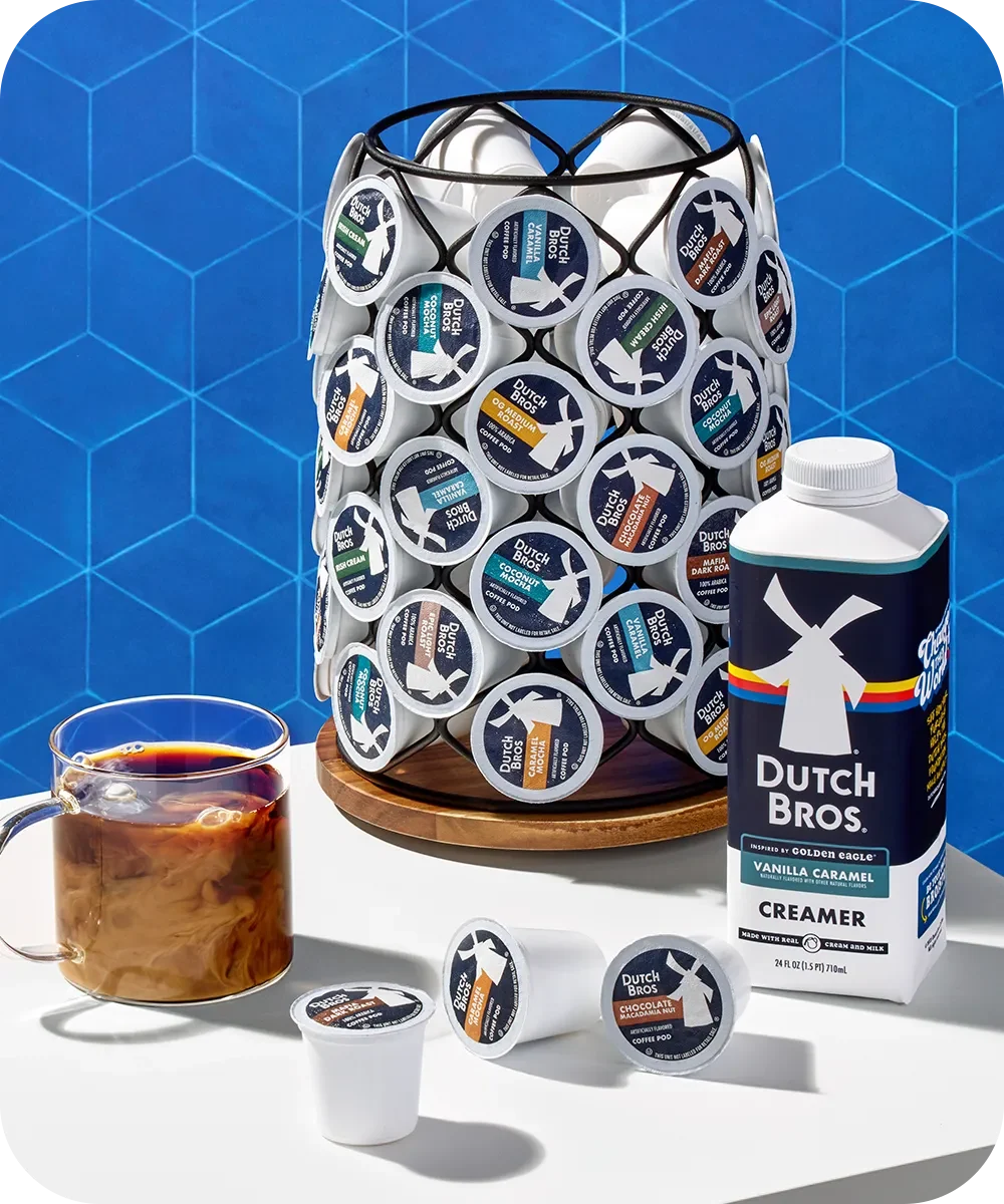 Dutch Bros coffee pod storage rack with coffee cup and vanilla caramel creamer against blue geometric background.