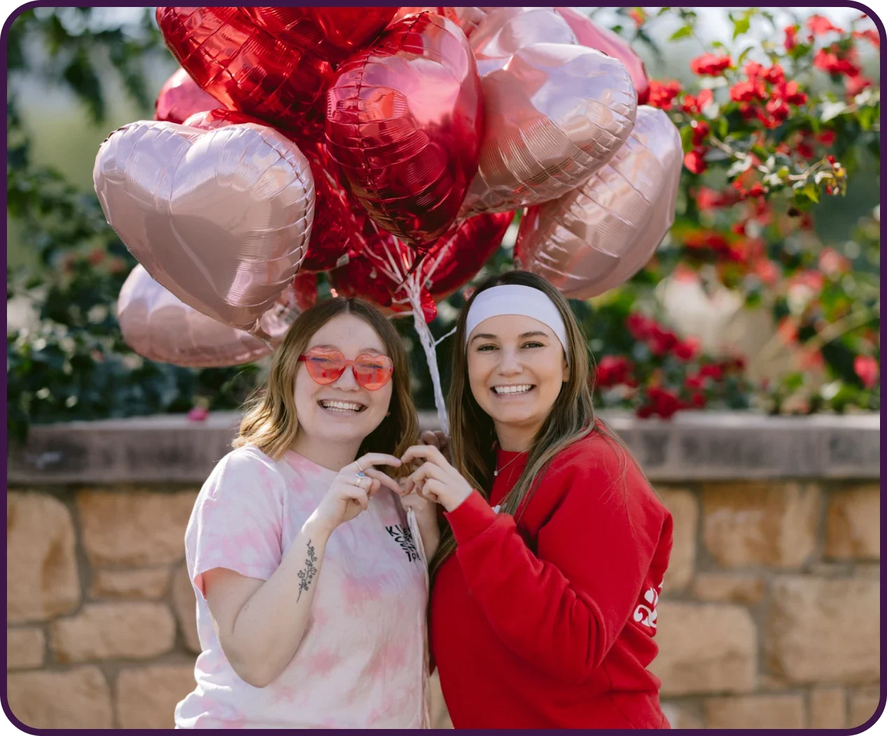 broistas making a hand heart in front of heart shaped balloons 