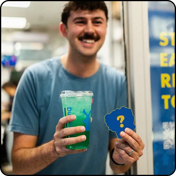 Smiling young man with a mustache holding a green Dutch bros drink and a mystery sticker.