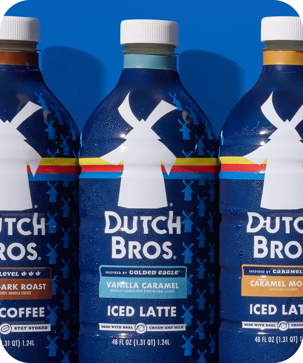 Three Dutch Bros bottled coffee drinks with different flavors including Vanilla Caramel Iced Latte against a blue background.