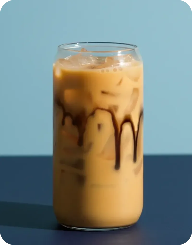 Tall glass of iced coffee with chocolate syrup drizzled inside the glass against a light blue background.